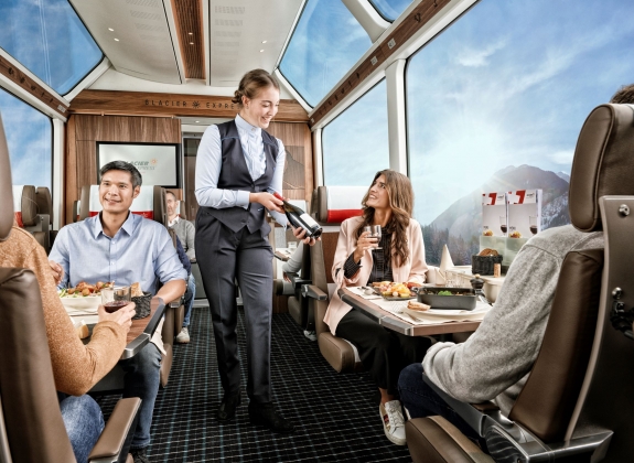 Glacier Express - Excellence Class Train staff serve onboard customers with drinks in luxurious carriage