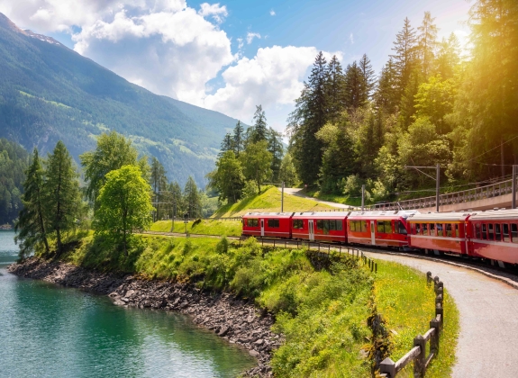 Red train moving along lake in beautiful mountain landscape in Switzerland