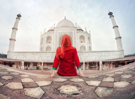 Woman in red costume sitting on the floor and looking at Taj Mahal in Agra, Uttar Pradesh, India