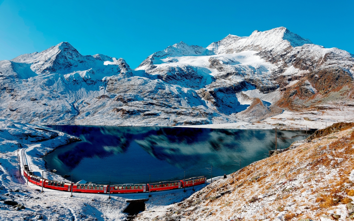 The Bernina Express at the Bernina Pass A train travels alongside a bright blue lake in winter
