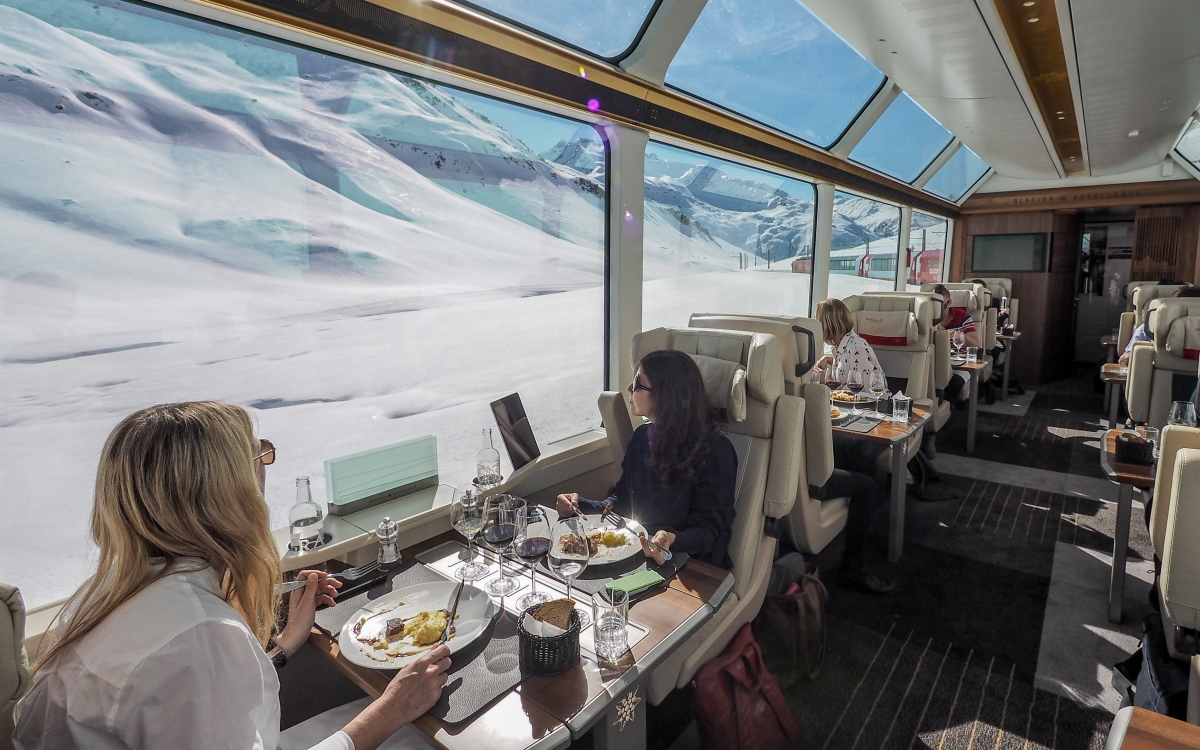 Onboard the Glacier Express - Excellence Class Train travellers look out of the window and the snowy Alpine scenery