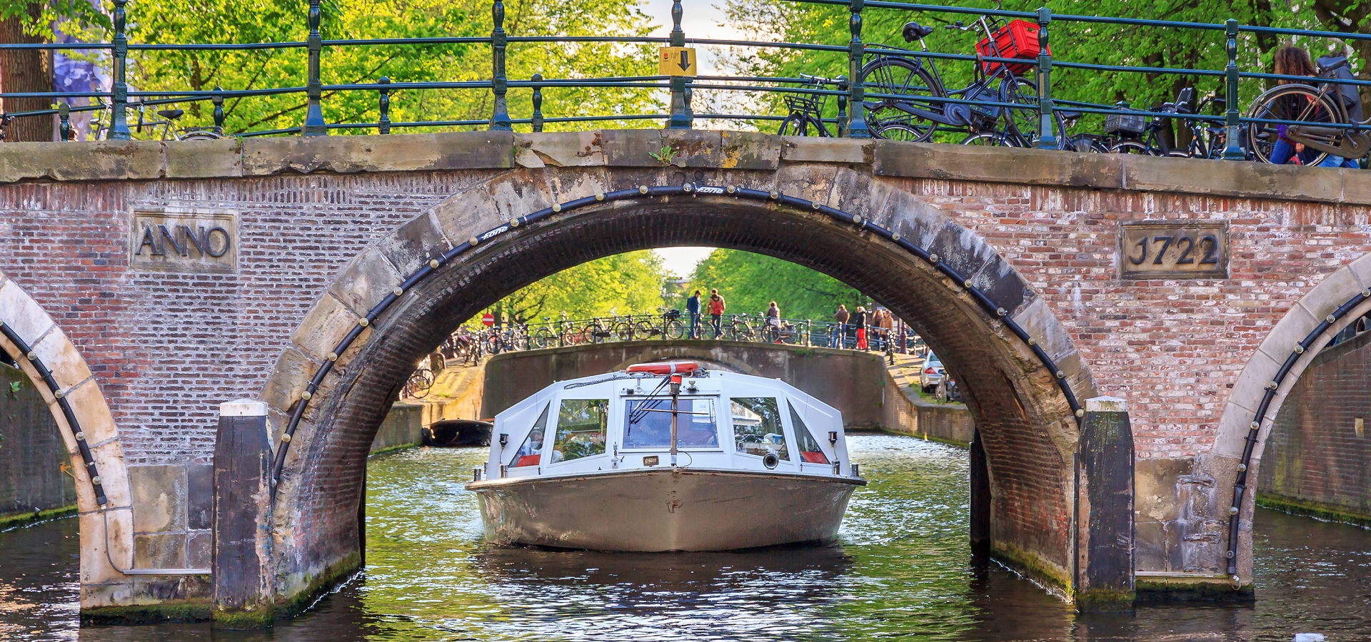 Canal cruise boat goes under the bridge over the Leidse canal at the Patricians' or Lords' canal (Herengracht) in Amsterdam in spring