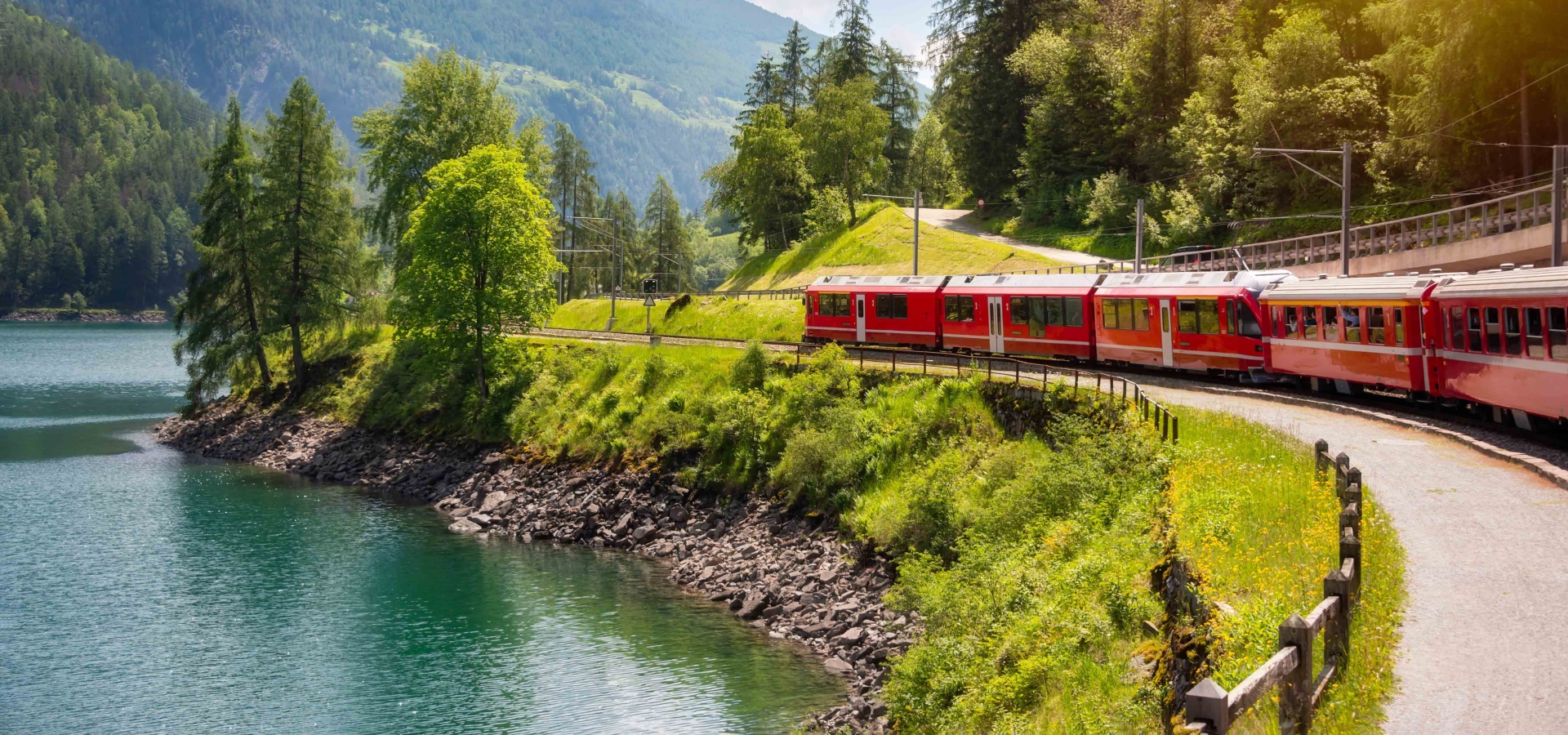 Red train moving along lake in beautiful mountain landscape in Switzerland