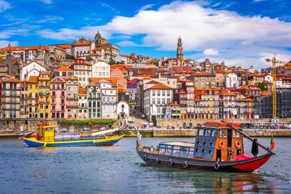 Wooden tour boats cruise the river in Porto, Portugal with the colorful city skyline in the background