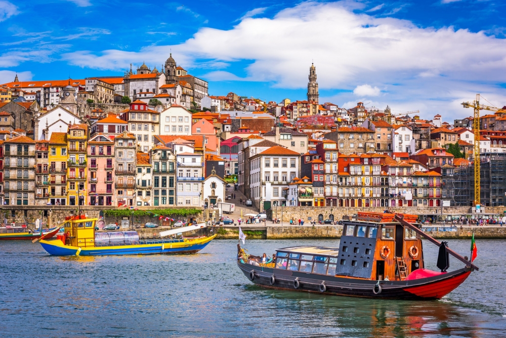Wooden tour boats cruise the river in Porto, Portugal with the colorful city skyline in the background