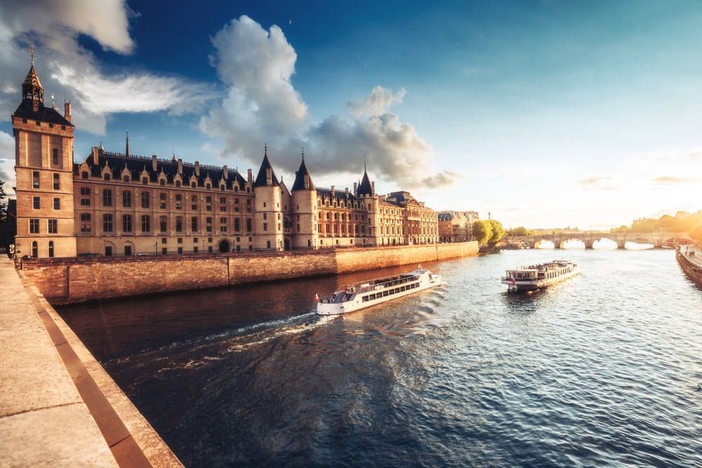 Dramatic sunset over river Seine and Conciergerie in Paris, France, with cruise boats and Pont Neuf. Colourful travel background. Romantic cityscape.