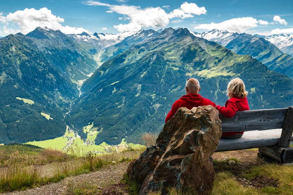 healthy and vital senior couple sitting on bench in austrian alps with beautiful view