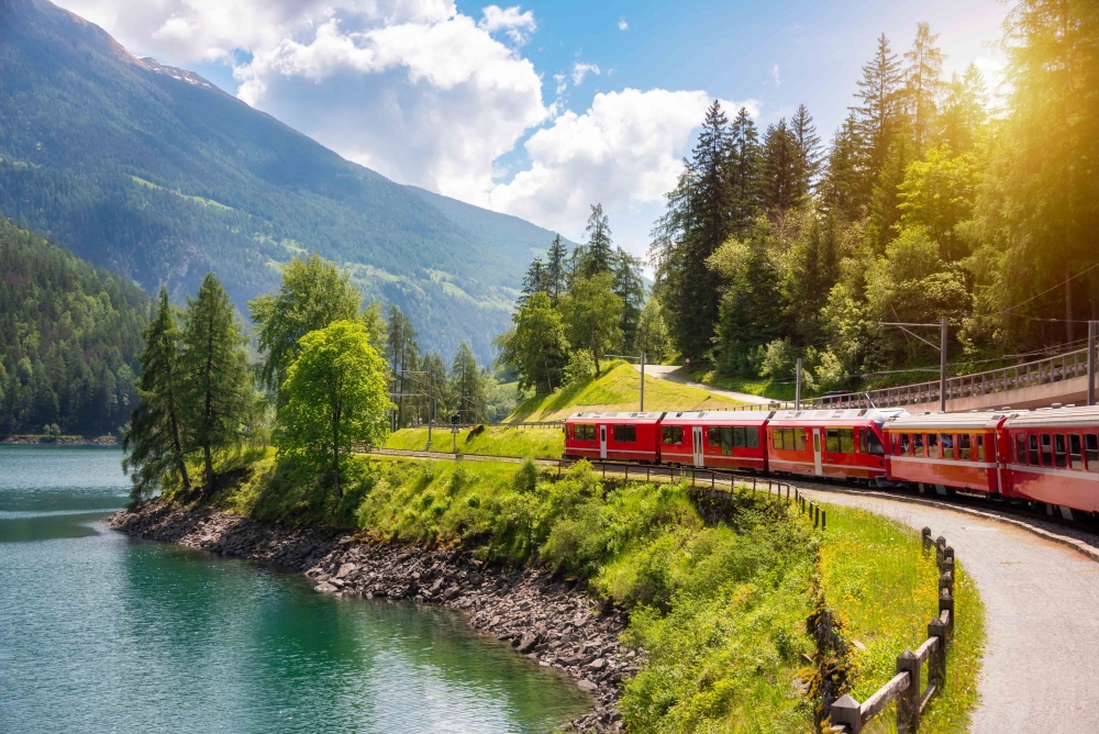 Red train moving along lake in beautiful mountain landscape in Switzerland