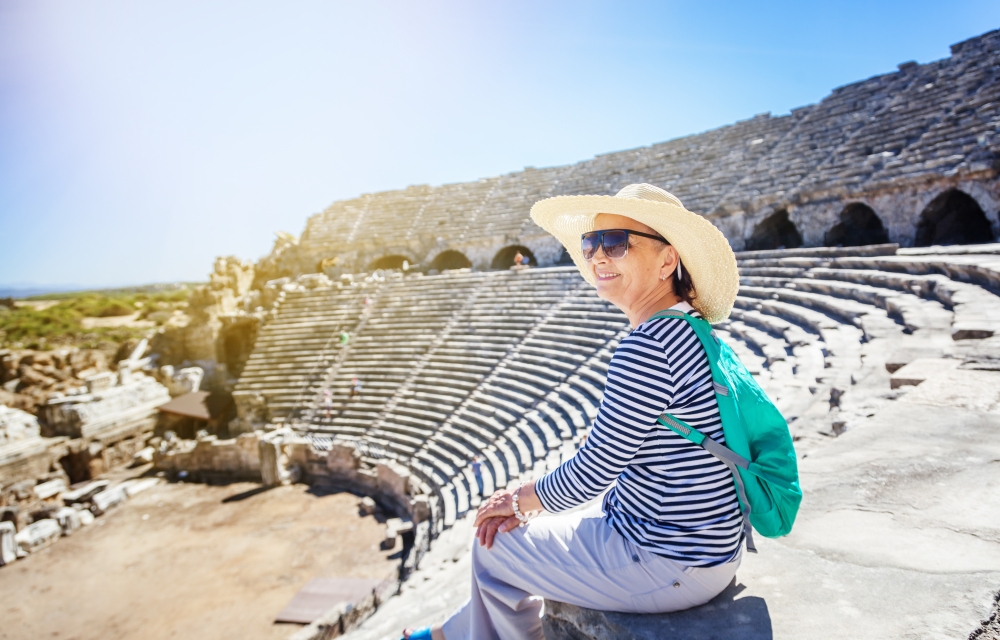Mature beautiful woman traveler, sits on the steps of the amphitheater in admiring the view